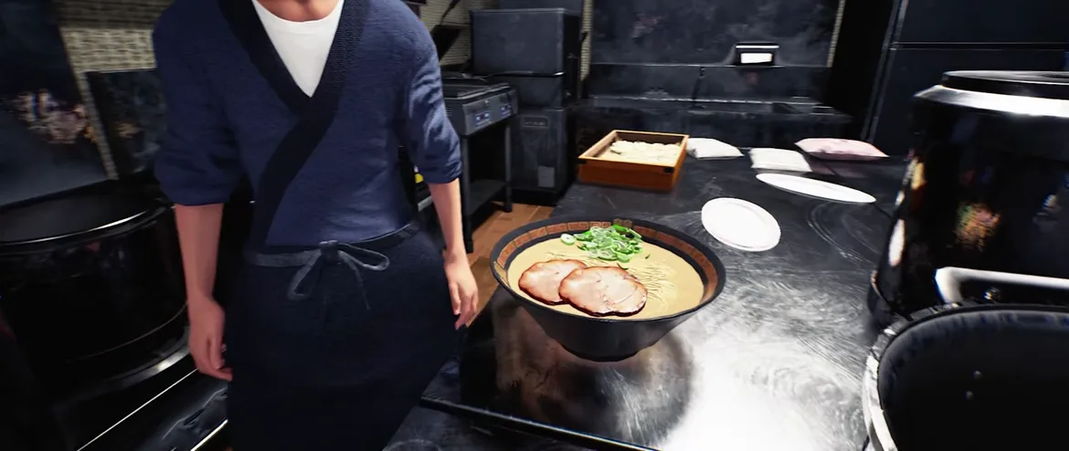 Japanese Ramen Simulator a character in a navy samue work jacket and black apron standing beside a black pass counter with a finished bowl of ramen topped with two chashu slices and scallions, wooden noodle box and stacked plates behind
