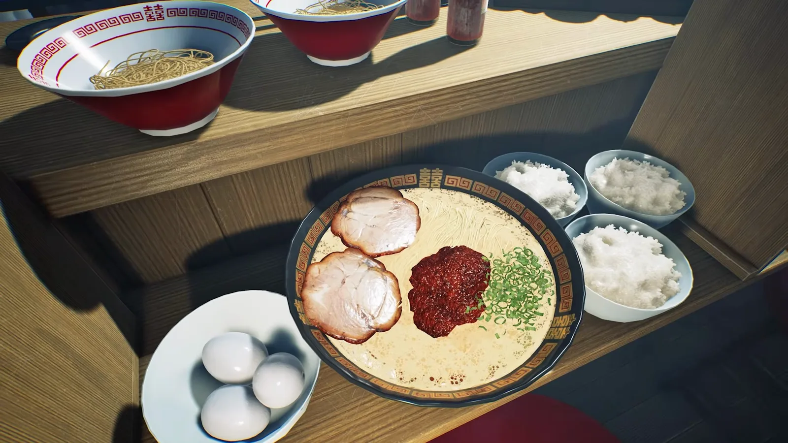 Overhead of a loaded Japanese Ramen Simulator service pass at 0:23: a black-and-gold bowl of pale broth with two chashu slices, a mound of red chili seasoning and chopped scallions, three small bowls of white rice, a plate of three peeled boiled eggs and two red bowls of plain boiled noodles