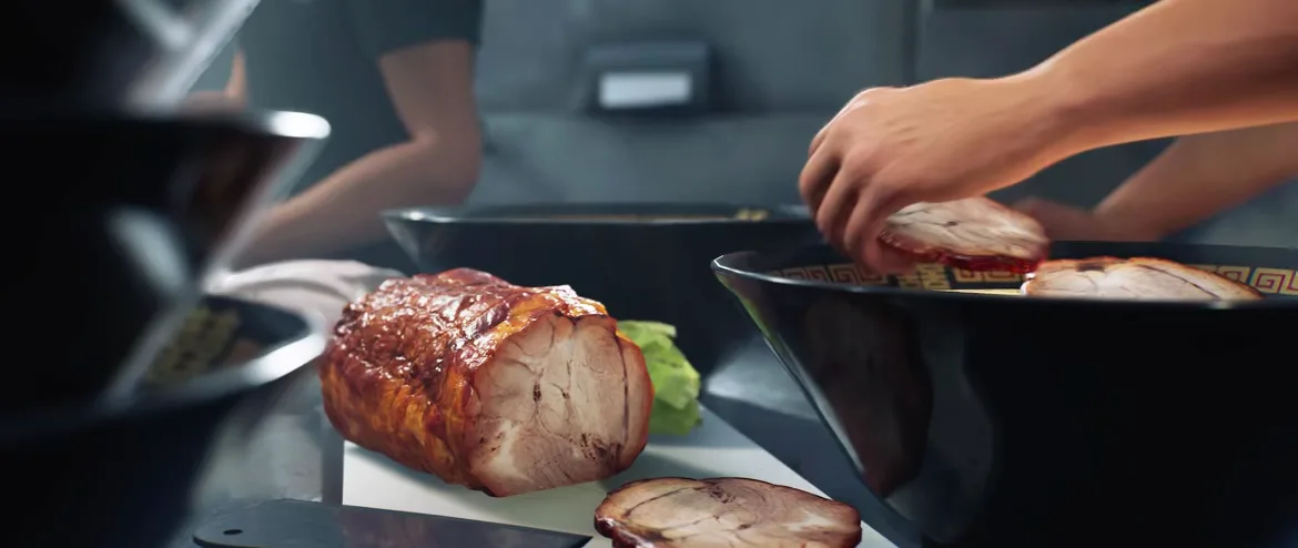 Japanese Ramen Simulator prep station with a glazed chashu pork roast on a white cutting board and a hand placing a chashu slice into a black bowl with a red key-pattern rim Japanese Ramen Simulator prep station with a glazed chashu pork roast on a white cutting board and a hand placing a chashu slice into a black bowl with a red key-pattern rim